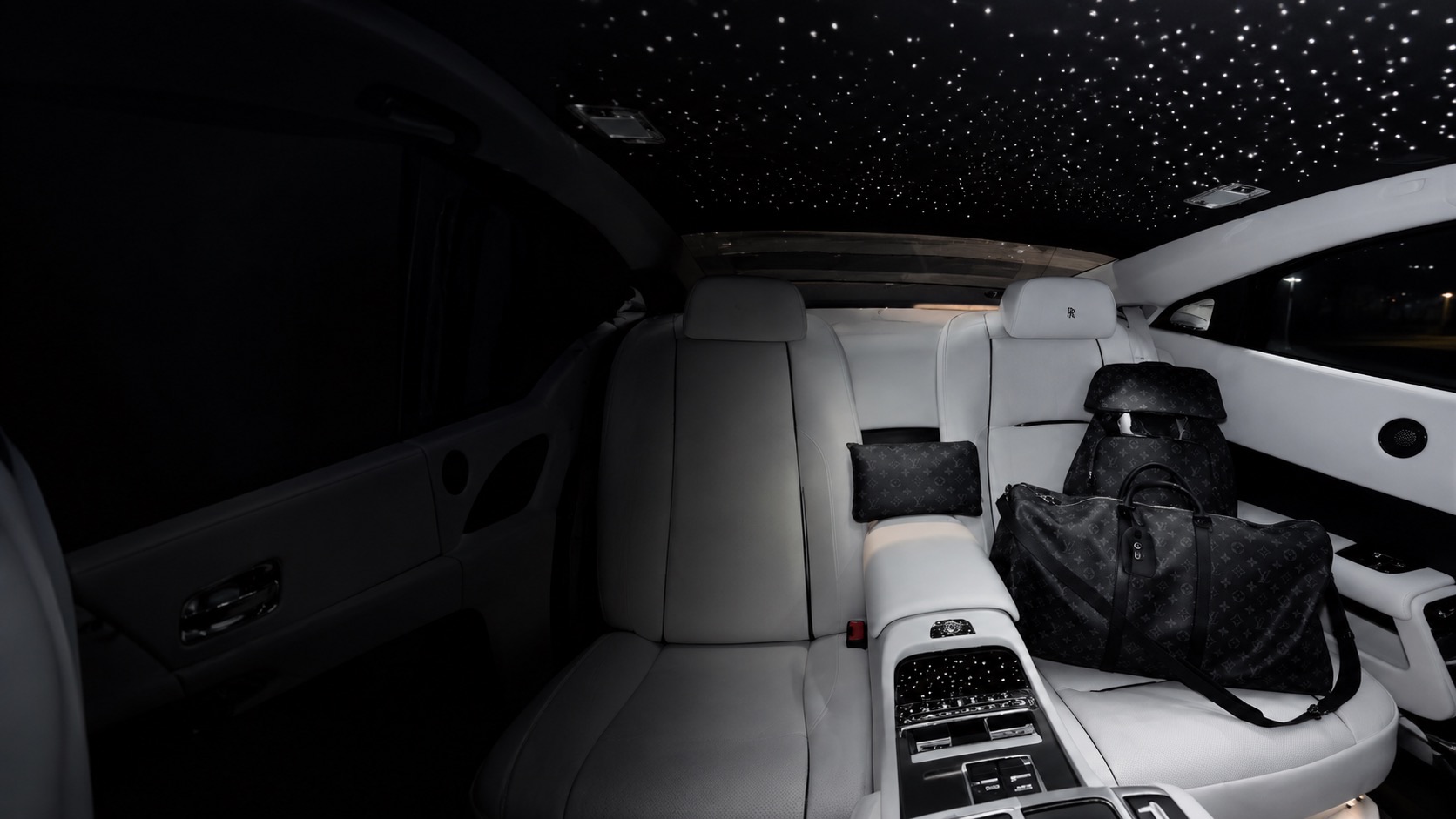 A white Rolls-Royce rear cabin under a starlight ceiling, with black monogram bags on the seat